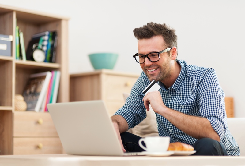Happy man sitting on sofa with laptop and credit card